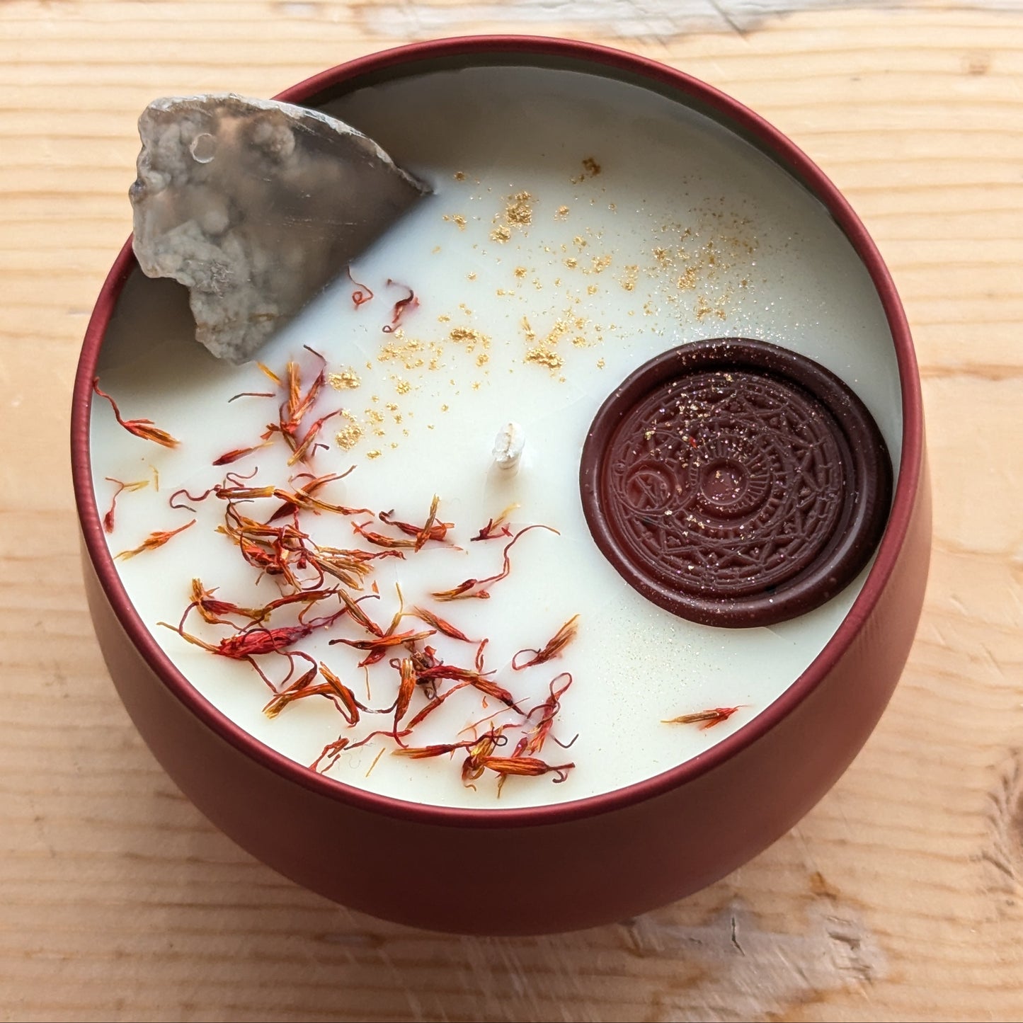 Candle in a 7oz container with an agate slice and dried safflower petals on a wooden surface